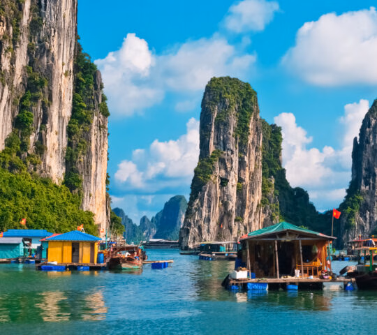 Vibrant floating houses and boats on the water surrounded by massive limestone cliffs in Halong Bay, Vietnam.