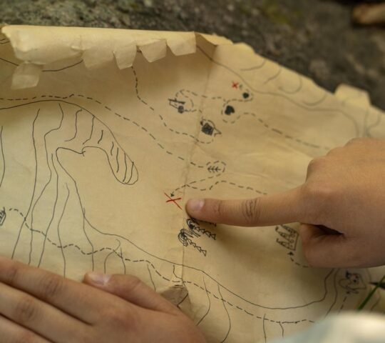 Close-up of hands pointing to a location marked with a red cross on a crinkled paper map.