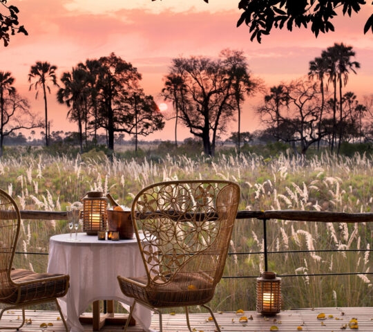 Table for two with champagne and lanterns on a deck overlooking the Botswana savanna at Sandibe Okavango Safari Lodge.