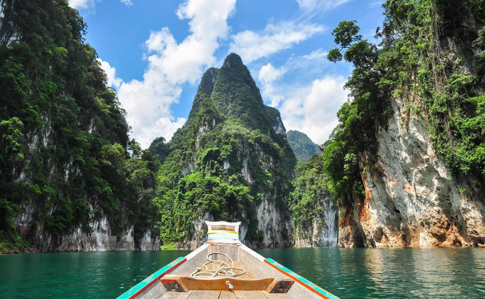 The prow of a wooden boat sailing across Cheow Larn lake with limestone karsts ahead