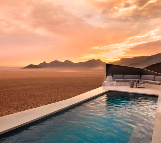 Private infinity pool and lounge area at Sossusvlei Desert Lodge overlooking a desert valley under a sunset sky.