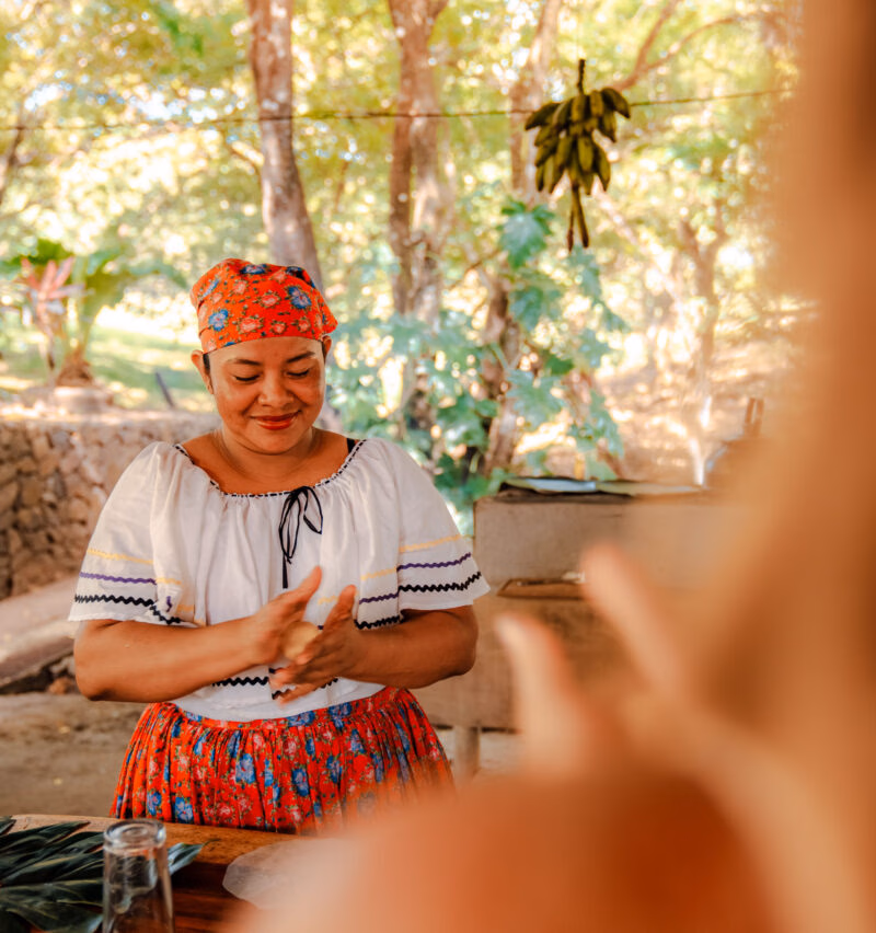 A woman in traditional Guanacaste dress rolls a tortilla and smiles during a cooking class.