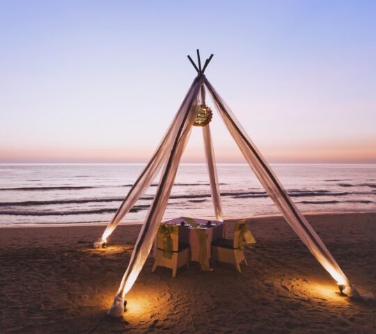 A romantic private dinner set up on a beach at sunset