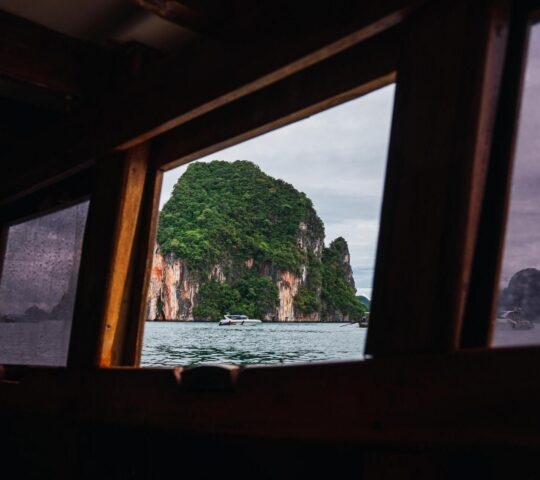 View from inside a boat out onto Phang Nga Bay with limestone cliffs and another boat in the distance