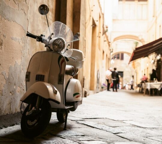 A cream coloured Vespa parked down a cobbled side street in Rome