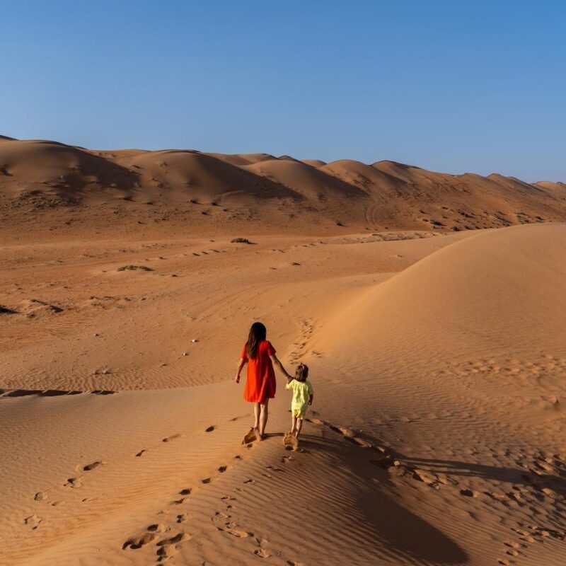 A mother and child walking along the sand dunes in Wahiba Sands, Oman