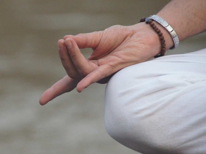 Close-up of a hand in Gyan Mudra position resting on a knee, featuring the thumb and index finger touching.