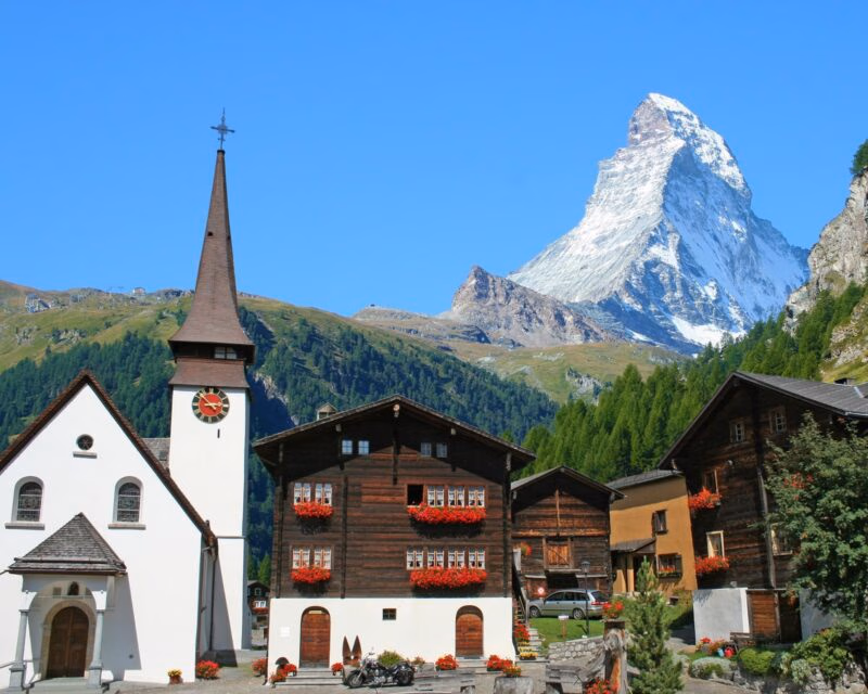 A white church and dark wood houses in Zermatt village with the iconic Matterhorn peak rising behind them.