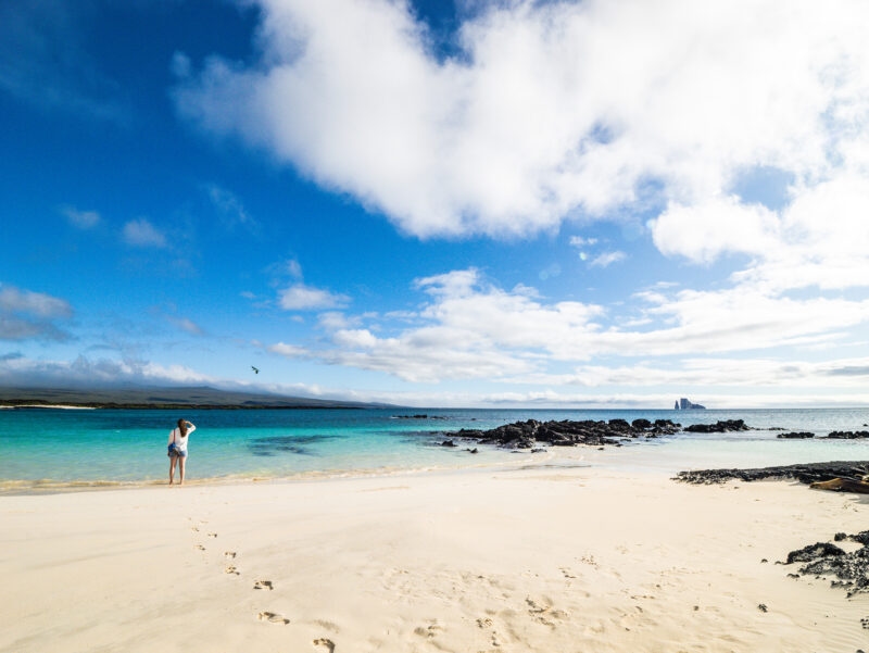 A person looking out at the turquoise ocean from a wide white sand beach on San Cristobal Island, Galapagos.