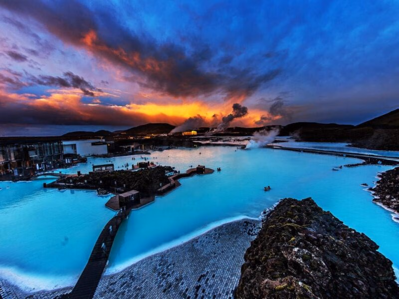 Geothermal spa with milky blue water and rising steam under a vibrant orange and purple sunset sky in Iceland.