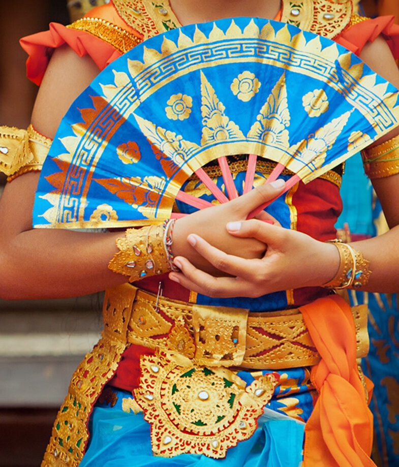 Close-up of two Balinese dancers in colorful traditional attire holding decorative blue and gold fans.