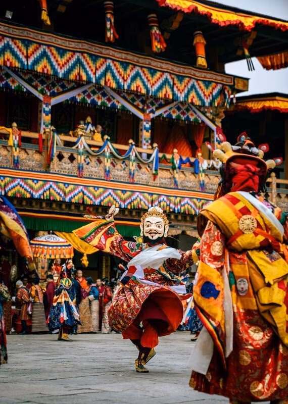 A dancer wearing a bearded mask and ornate robes performs in a courtyard.