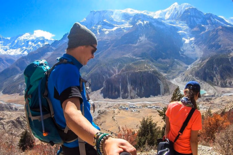 Two hikers overlooking a deep valley and massive snow-covered mountains.