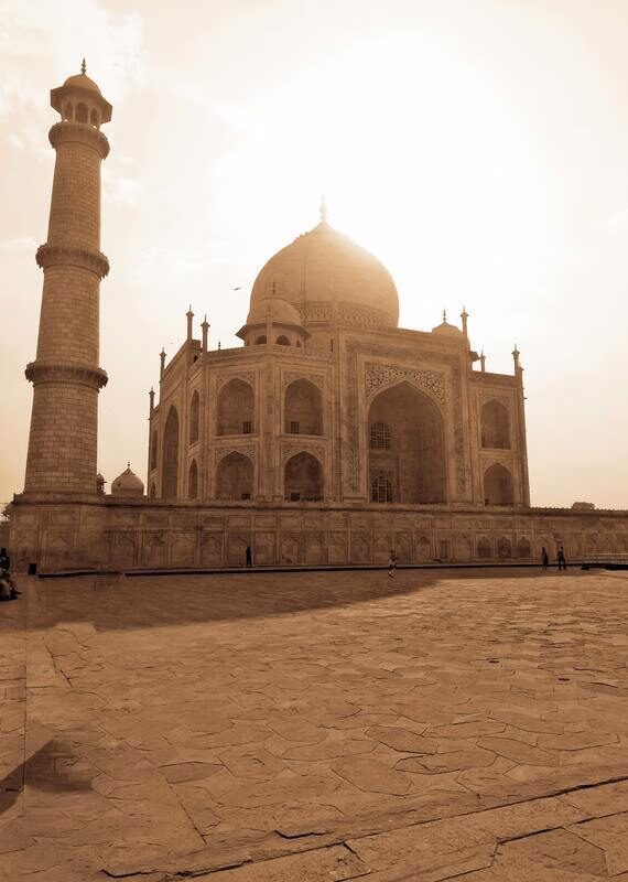 Sepia view of the Taj Mahal with a minaret on the left under a bright sky.