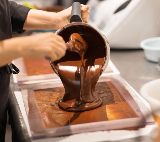 close up of a woman's hands pouring melted chocolate from a bowl into a mould to make bars