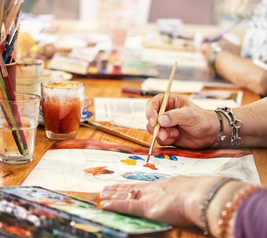 Close up of a woman's hands holding a paintbrush to work on a watercolour painting