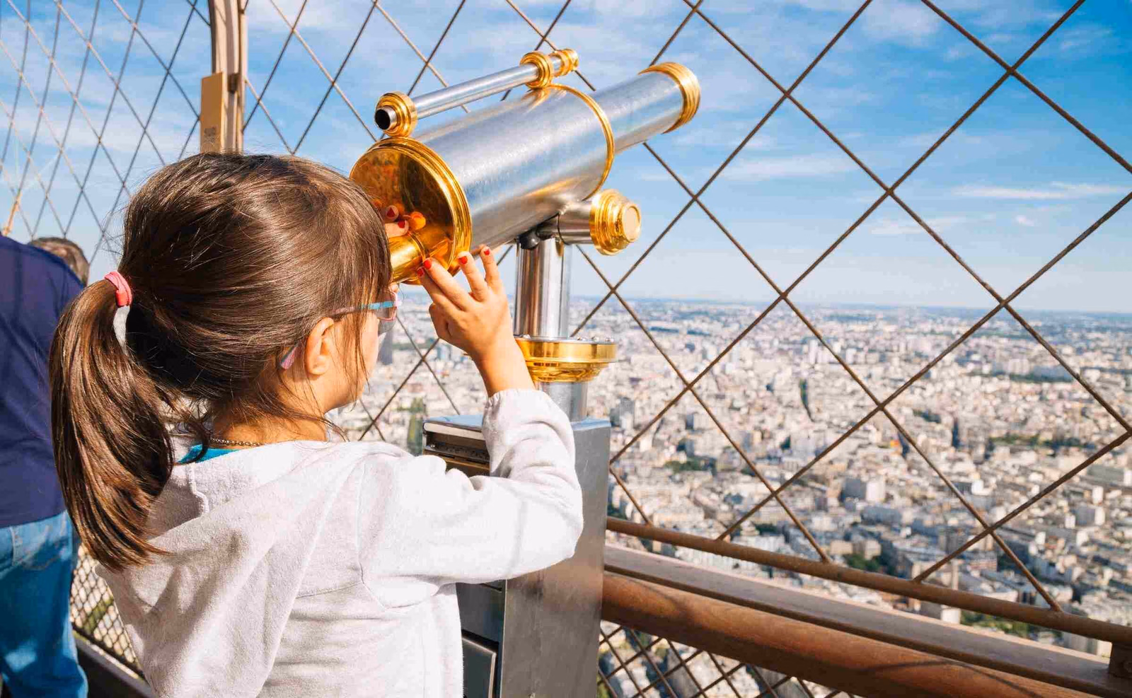 A little girl looking through a telescope at the Paris skyline on the viewing platform at the top of the Eiffel Tower
