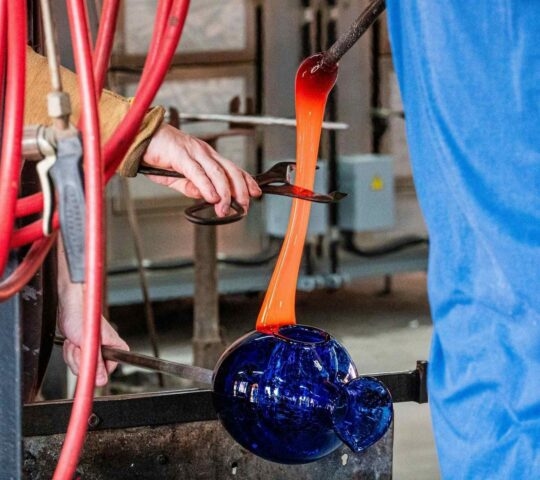 Inside a glassmaking workshop with a man making a blue vase