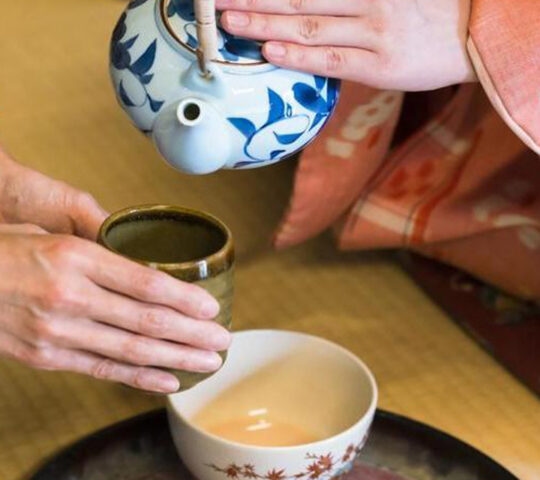 A woman in a colourful kimono pours green tea during a Japanese tea ceremony.