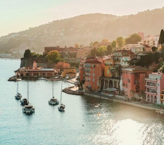View of Villefranche sur mer on the French Riviera with sunlight glinting on the water and small yachts docked in the hrabour