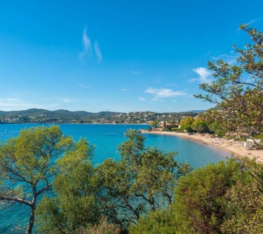 View of a golden sandy beach at Saint-Raphael on the French Riviera, with turquoise sea and green trees