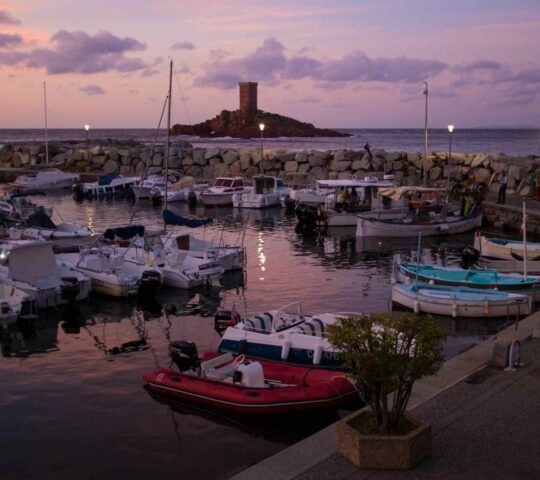 A small harbour in the French town of Saint-Raphael at sunset with a rocky outlet with stone tower in the background