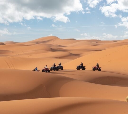 A group of people riding ATVs through sand dunes in the Moroccan Sahara