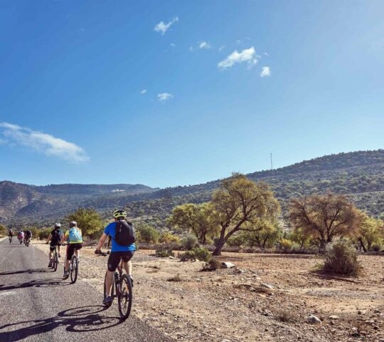 A group of people cycling on a flat road with desert scenery and mountains at the side
