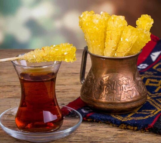 A glass of saffron tea with sticks of crystalised sugar for stirring