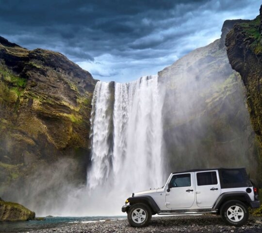 A super Jeep stopped in front of a cliff with a waterfall in Iceland