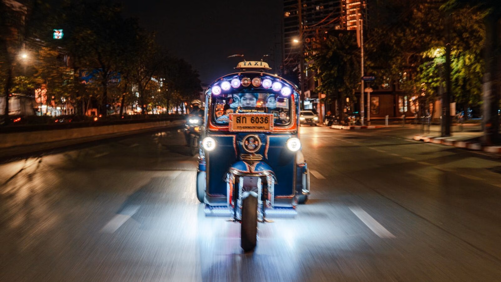 A Bangkok tuk tuk with bright lights on an empty evening road.