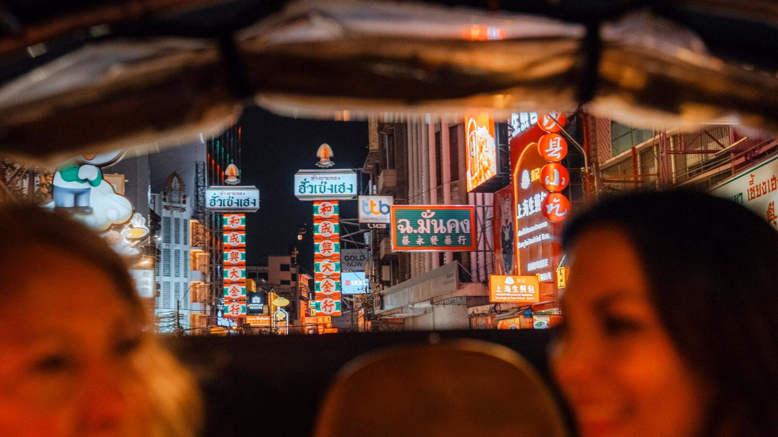 Bangkok's Chinatown brightly lit and colourful street signs with a mother and daughter in the foreground enjoying a private tuk tuk ride.
