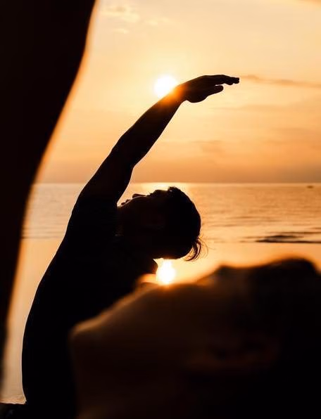 A private sunrise yoga experience as a yoga teacher raises their arm in the sunlight.
