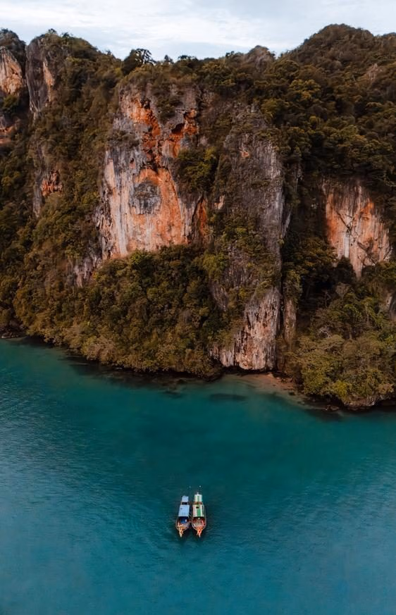 An aerial view of two long tail boats in front of limestone cliffs and turquoise ocean
