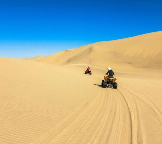 Two people driving quadbikes over sand dunes