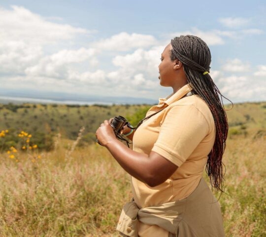 A female safari guide holding binoculars and looking overs the plains in search of animals