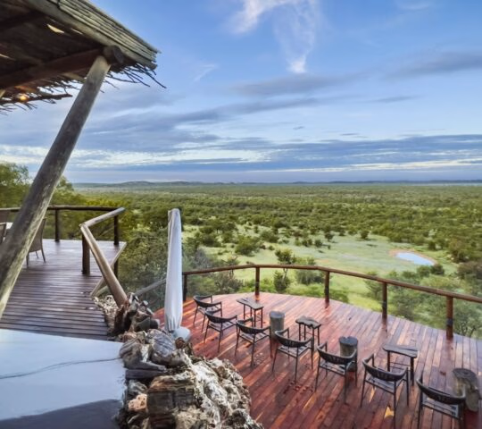 Wooden outdoor viewing deck at Ongava Lodge with chairs overlooking an expansive green savanna landscape.