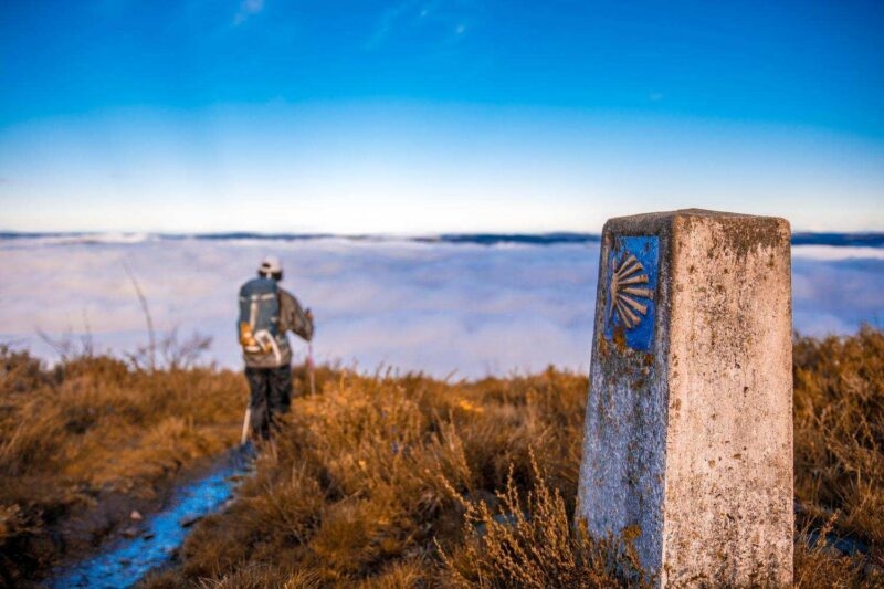 A man hiking past a marker on the Camino de Santiago