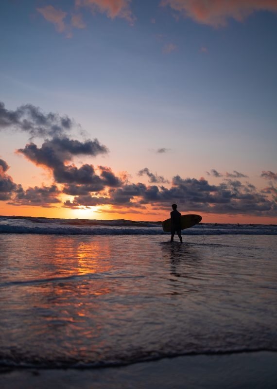 Silhouette of a surfer carrying a surfboard into the ocean at sunset during active costa rica.
