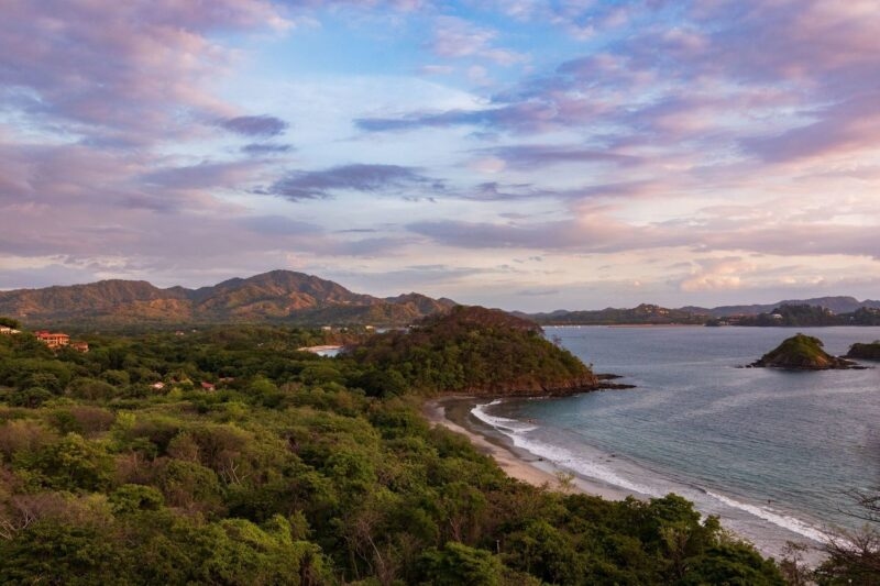 Sunset over a forested coastline with a sandy beach cove during Costa Rica adventure tours.