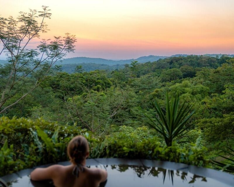 Person relaxing in an outdoor pool overlooking a lush jungle valley on Costa Rica adventure tours.