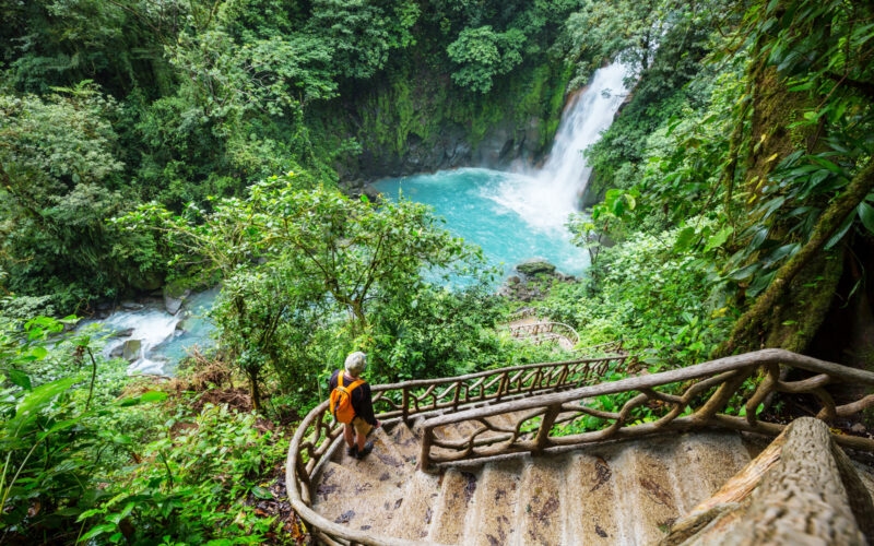 Hiker on steps viewing a bright blue waterfall in a lush jungle on Costa Rica adventure tours.