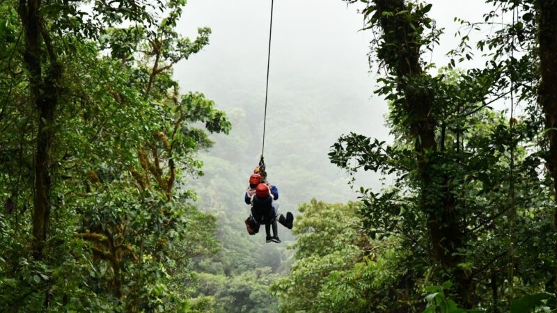 Two people tandem zip-lining through a misty green rainforest canopy on Costa Rica adventure tours.