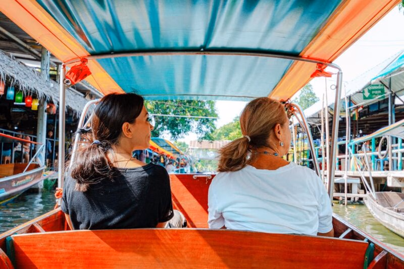 Two women on a family-trip sit in a wooden boat traveling down a canal past a green sign reading PIER.