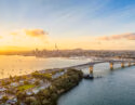 Aerial view of the Auckland skyline and Harbour Bridge at sunset during a family-trip, with boats on the golden water.