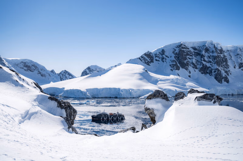 A black latin america expedition cruise ship floats in an icy bay surrounded by snowy mountains.