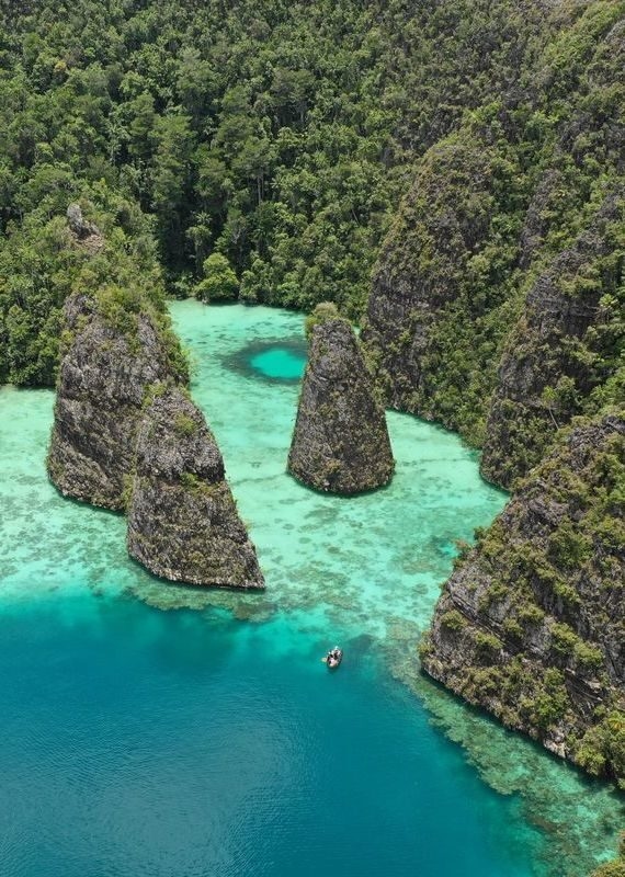 Aerial view of a small boat in clear turquoise water surrounded by steep, tree-covered limestone islands.