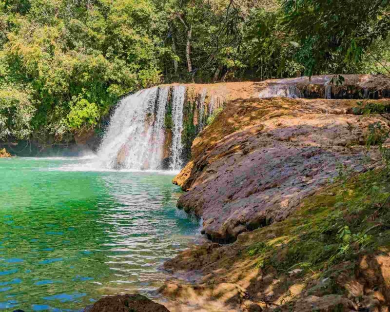 A small waterfall pouring into a green pool surrounded by rocks near Estancia Mimosa nature reserve in Bonito