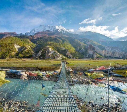 A suspension bridge lined with prayer flages over a river in Annapurna, Nepal
