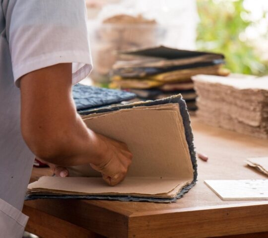 A person binds a handmade book on a wooden desk inside a paper-making studio in barichara colombia.
